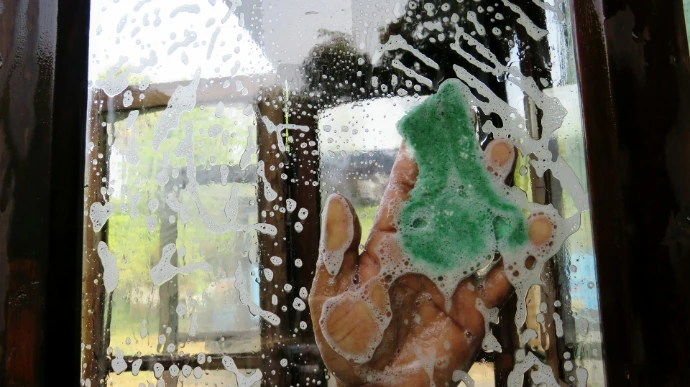a hand holding a green sponge in front of a window